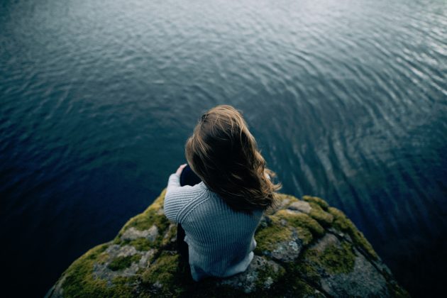 Girl sitting on a rock alone overlooking open water
